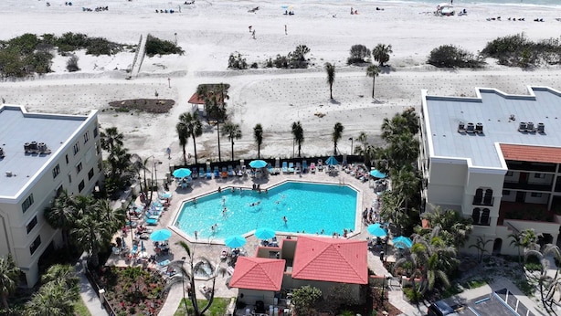 A resort with a swimming pool surrounded by lounge chairs and umbrellas, a beach in the background, and palm trees. - Beachfront Upgraded Condo. Beach Views! Pool, BBQ, Hot Tub, Volleyball & Shuffleboard, Parking (Treasure Island)
