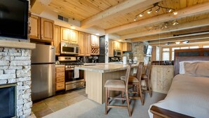 Une cuisine moderne avec des meubles en bois, une cheminée en pierre et un grand îlot central doté de tabourets de bar.