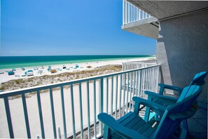 A balcony with a view of a beach, featuring a railing and two chairs.