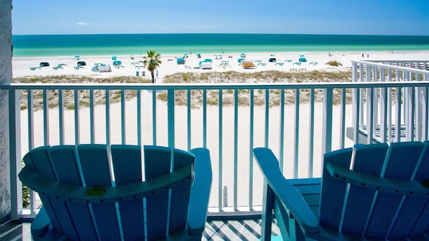 Ein Balkon mit zwei blauen Stühlen mit Blick auf einen Strand mit türkisfarbenem Wasser und weißem Sand.