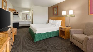 Habitación de hotel con cama, una silla, un escritorio, televisión, espejo y un cuadro en la pared.