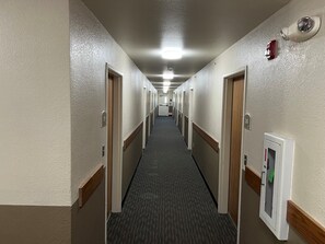 Ein Hotelgang mit Teppichböden, Türen auf beiden Seiten und einem Rauchmelder rechts.
