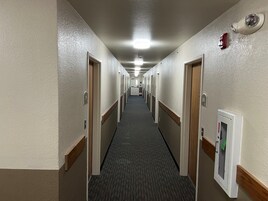 Un pasillo de hotel con pisos alfombrados, puertas a ambos lados y un detector de incendios a la derecha.