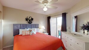 Un dormitorio con cama, mesita de noche, cómoda, ventilador de techo y ventana con cortinas.