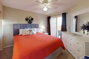 A bedroom with a bed, a nightstand, a dresser, a ceiling fan, and a window with curtains.