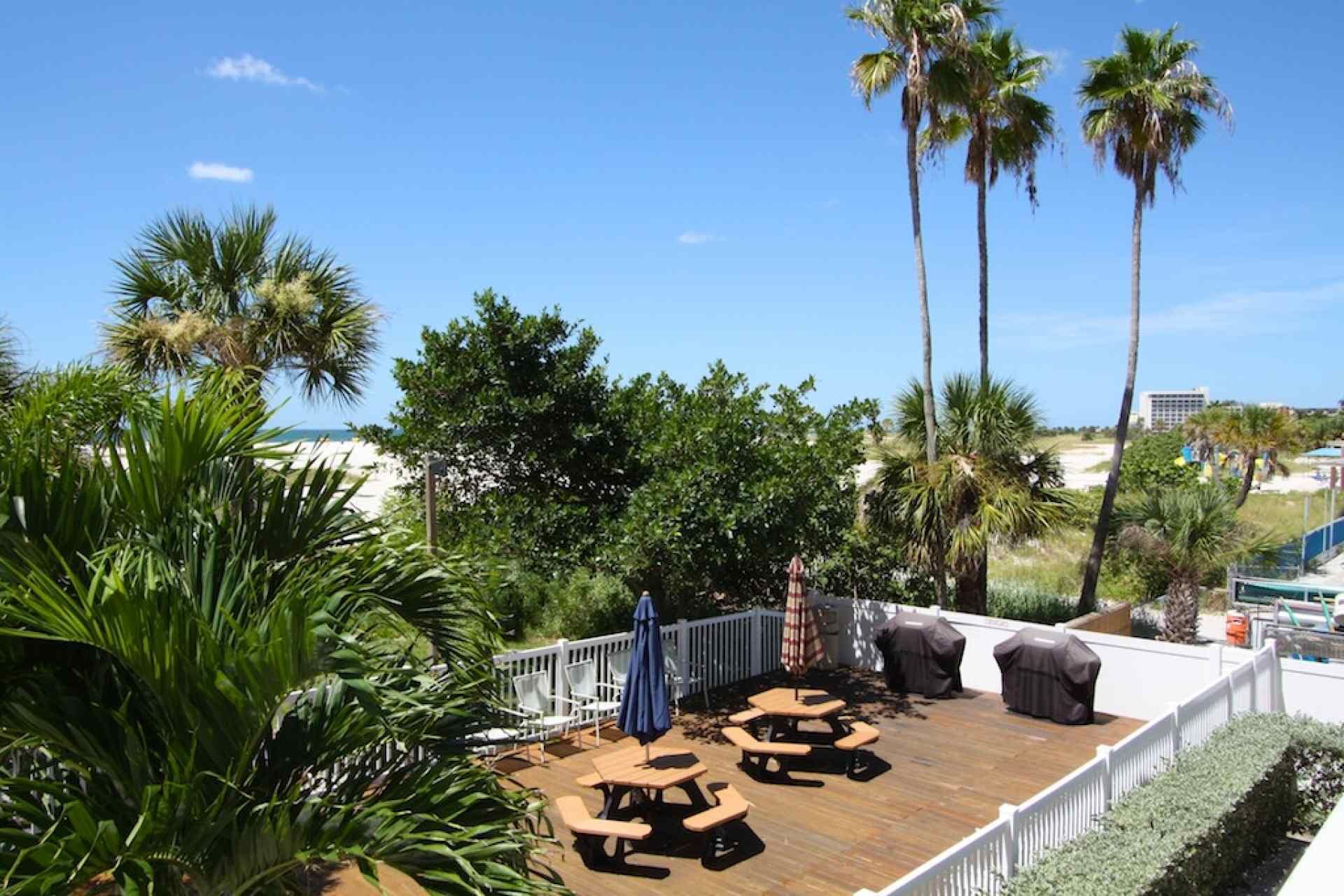 A deck with outdoor seating, surrounded by palm trees and a view of the beach.