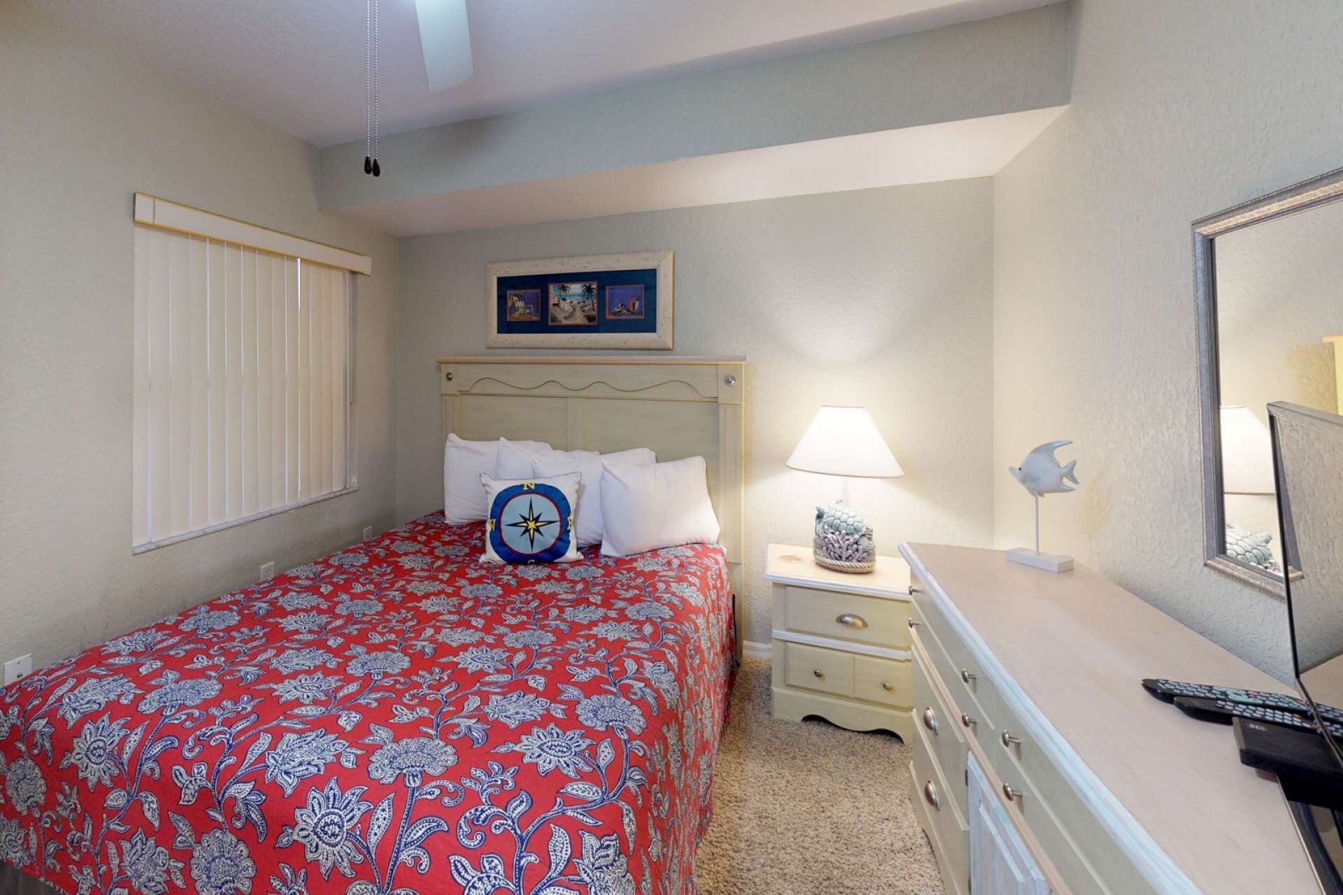 A bedroom with a bed, bedside table, lamp, and dresser.