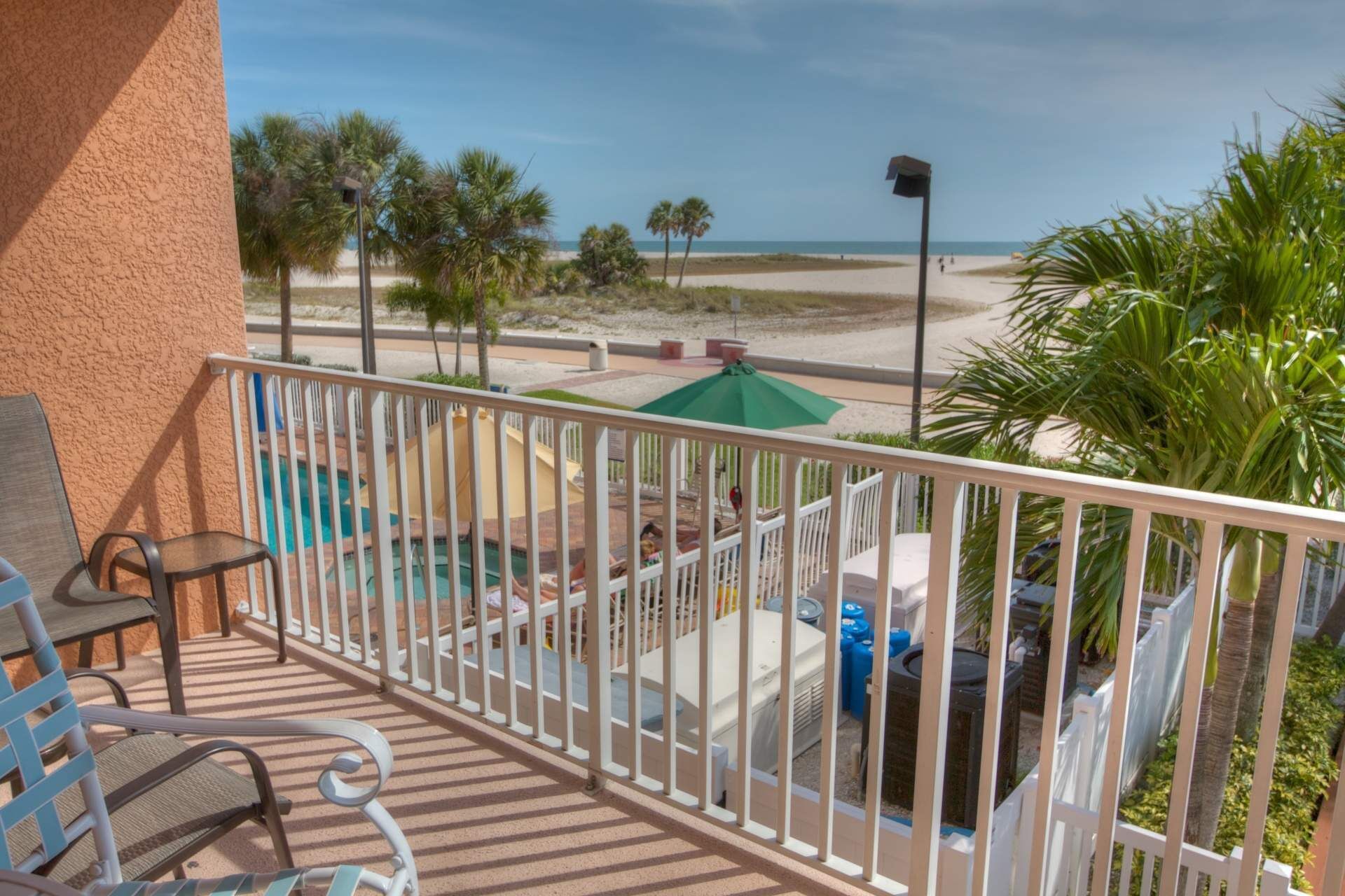 A balcony with a pool, chairs, and a view of the beach.
