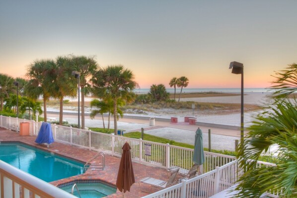 A pool area with a view of the beach and ocean during sunset.