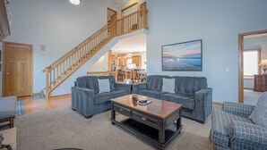 A spacious living area with a grey sofa set, a wooden coffee table, and a staircase leading to an upper floor. - Outdoor Hot Tub, Pool Table, Huge Fire Pit - Close 2 Pools! (Galena)