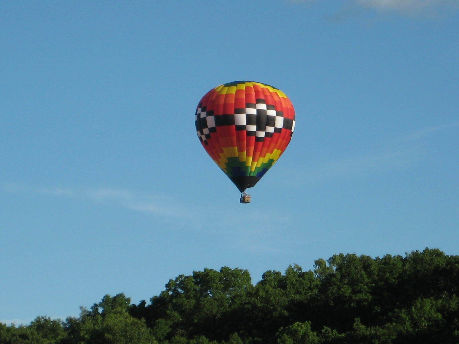 A hot air balloon with a checkered pattern, flying above a forested area.