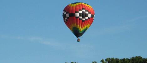 A hot air balloon with a checkered pattern, flying above a forested area.