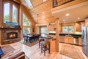 A spacious kitchen with wooden cabinets, a stone fireplace, and large windows.