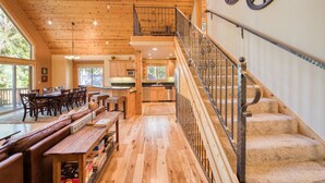 Un interior espacioso de madera con comedor, cocina y una escalera que sube a un nivel superior.