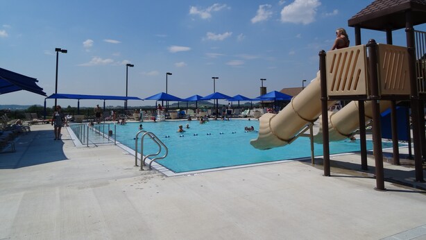 A swimming pool with a slide, blue umbrellas, and a lifeguard tower.