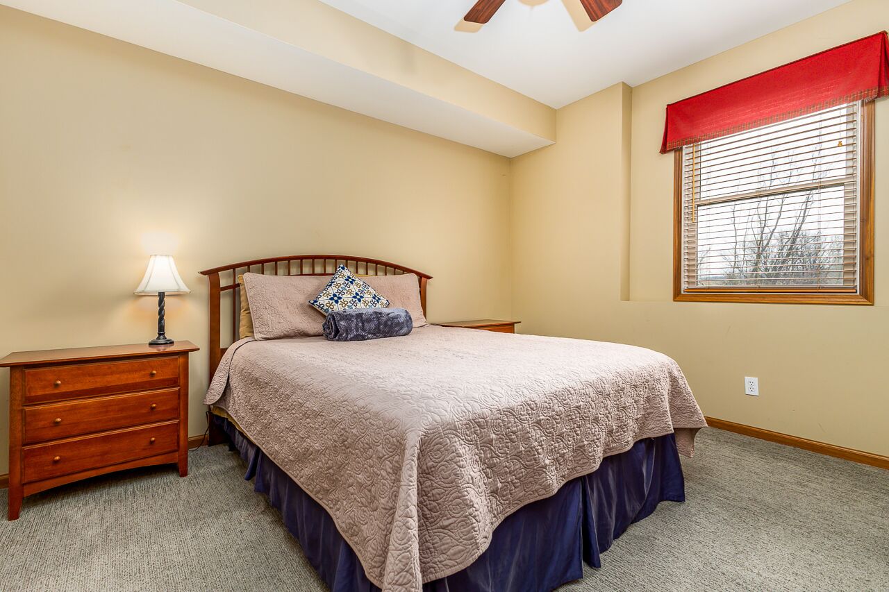 A bedroom with a bed, nightstand, lamp, and window with blinds.