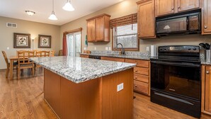 A kitchen with wooden cabinets, a granite countertop, a built-in oven, and a dining area with chairs.