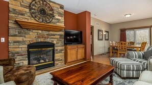 A living room with a stone fireplace, a flat-screen TV, a wooden coffee table, and striped sofas.
