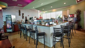Un ristorante con area bar, posti a sedere e un frigorifero.