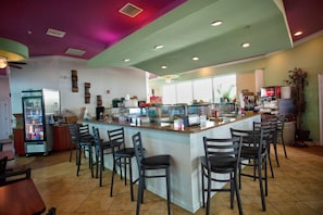 A restaurant with a bar area, seating, and a refrigerator. - Beachfront Resort. Corner Unit w/ 2  Balconies - Partial Beach View. Cafe, Gym, Bar, Pool & Hot Tub. (Treasure Island)