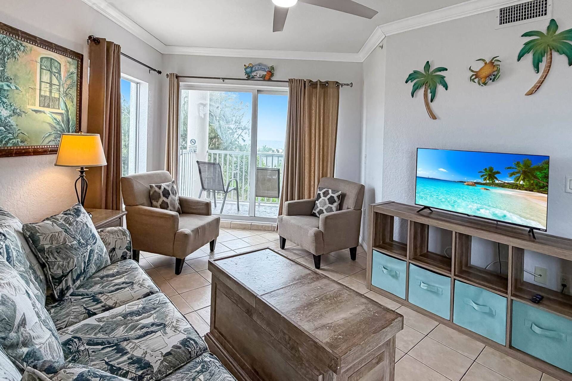 Een woonkamer met een bank, fauteuils, een salontafel, een televisie en een balkon met gordijnen.
