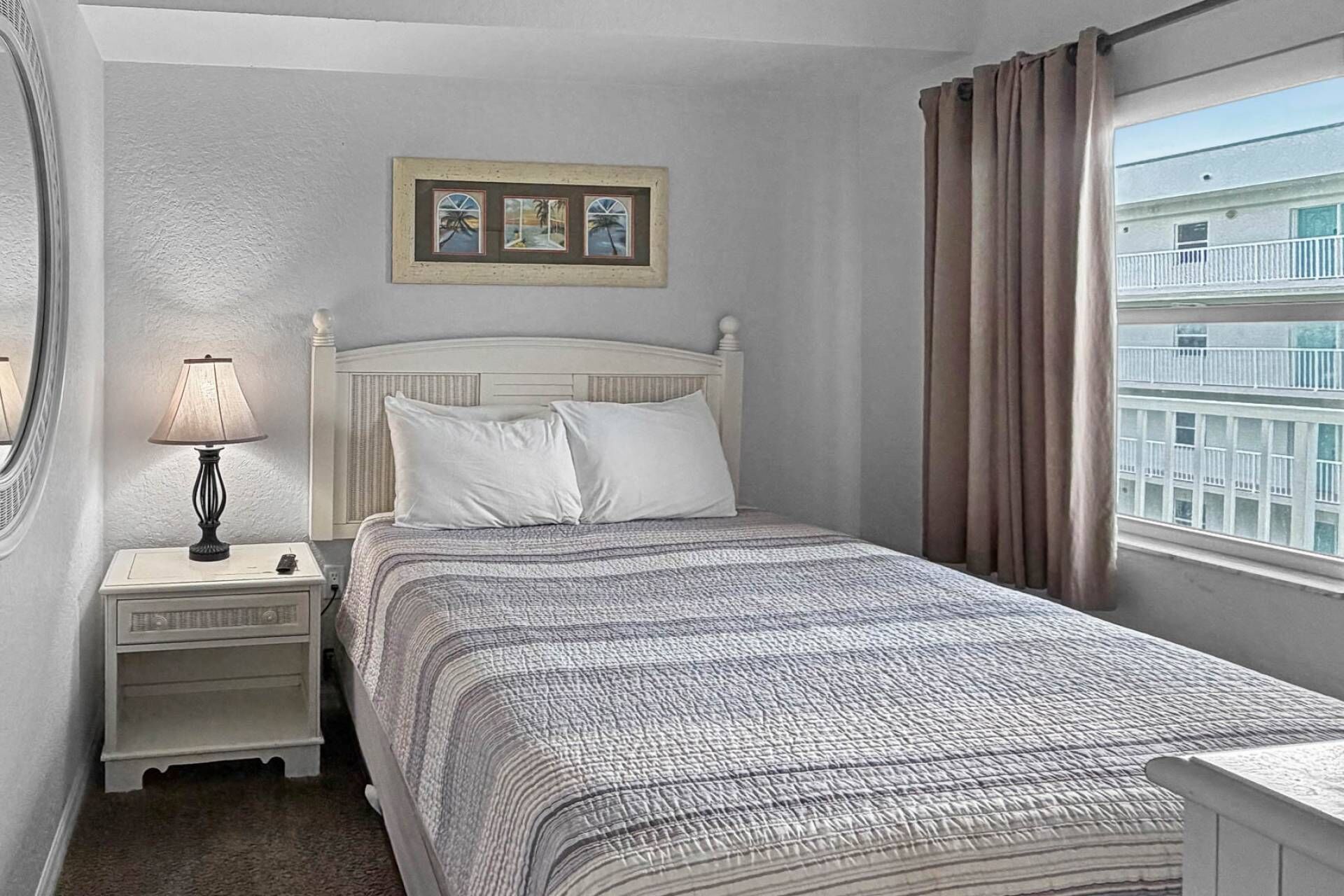 Uma cama bem arrumada com colcha estampada, uma luminária de cabeceira, mesa de cabeceira e um quadro emoldurado acima da cama.