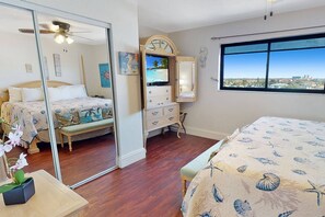 A bedroom with a bed, a dresser, a mirror, and a window with a city view.