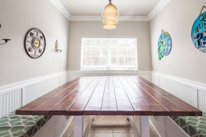 Un comedor con una mesa de madera, paneles blancos, una ventana con persianas y adornos en la pared.