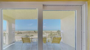 A balcony with two yellow chairs and a table, overlooking a beach with a clear sky. - Modern 2Br/2Ba Beachfront Condo with an Incredible View. Amenities, Pool, Beautiful Beach (Treasure Island)