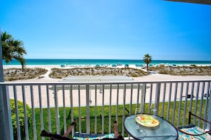 A balcony with a view of a beach, featuring a table with a plate and glass, and a chair.