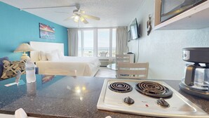 Una camera d'albergo con un letto, una scrivania con un computer, una macchina del caffè e vista sull'oceano.