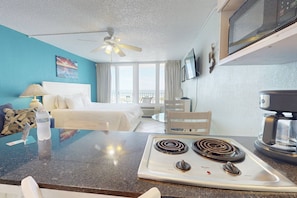 A hotel room with a bed, a desk with a computer, a coffee maker, and a view of the ocean.