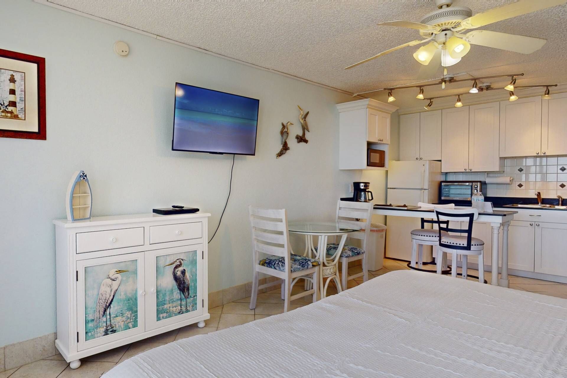 A compact room with a bed, a dining area with chairs, a small kitchen with a microwave and coffee maker, and a ceiling fan.