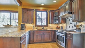 Une cuisine avec des meubles de couleur sombre en bois, un plan de travail en granit, une grande fenêtre et une cuisinière en acier inoxydable.