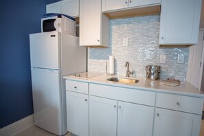 A kitchen with white cabinets, a stainless steel sink, a microwave, and a tiled backsplash.