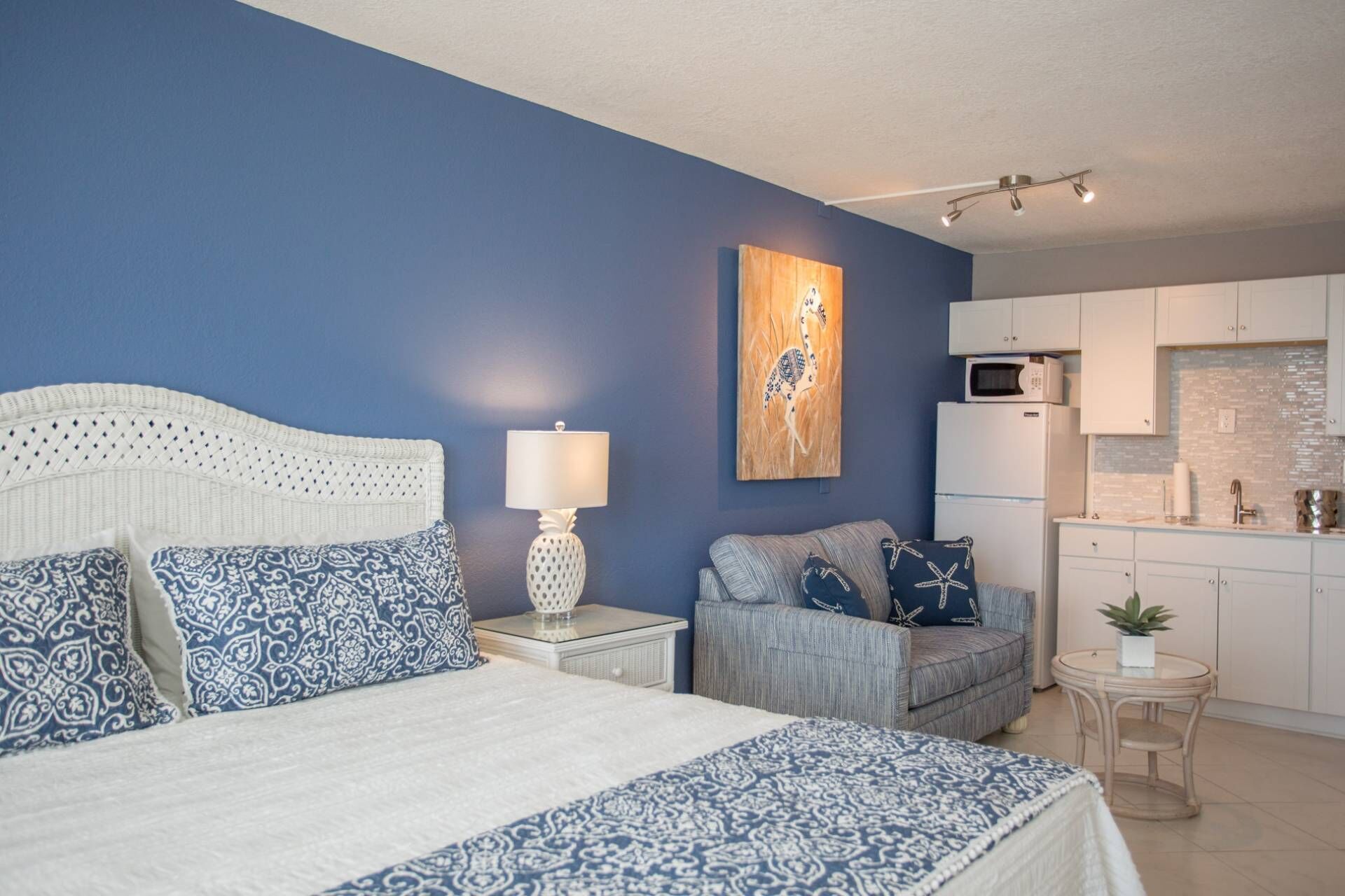 A bedroom with a bed, nightstand, lamp, and a wall-mounted artwork.