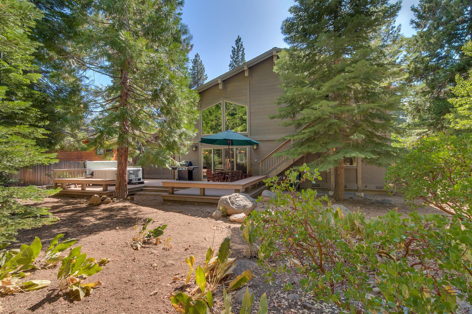Una casa moderna con un patio, mobiliario exterior y un árbol grande al frente.
