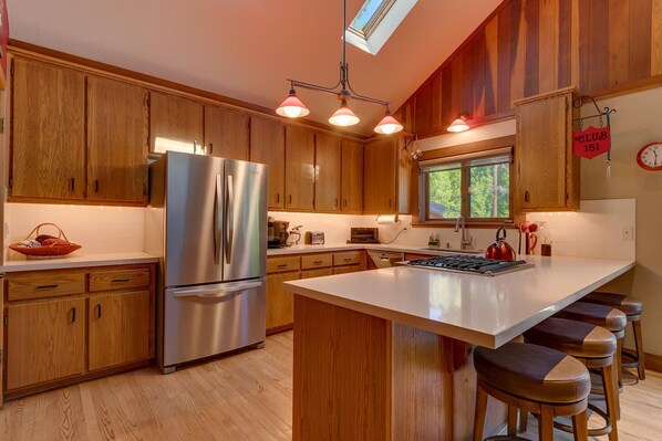 Cocina moderna con armarios de madera, refrigerador de acero inoxidable, una isla grande con taburetes e iluminación colgante.