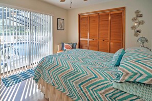 Een slaapkamer met een groot bed, een houten kledingkast en uitzicht op een zwembad door een raam met zonwering.