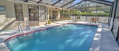 A covered swimming pool with a patio area, a covered seating area, and a view of the surrounding landscape.
