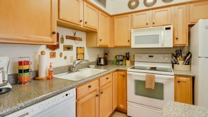 A kitchen with wooden cabinets, a white microwave, a stove, and a sink.