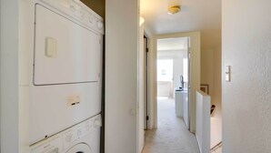 A laundry room with stacked washers and dryers, a hallway leading to a kitchen, and a door to another room.