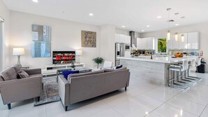 Una sala de estar moderna con un sofá, una mesa de centro y un televisor. Cuenta con una cocina con refrigerador, microondas y una mesa de comedor.