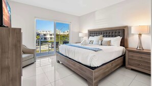 Un dormitorio moderno con una cama grande, una mesita de noche, una silla y vistas a la ciudad a través de un amplio ventanal.