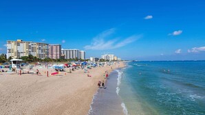 Una playa con una fila de hoteles, cielos azules despejados y gente disfrutando.