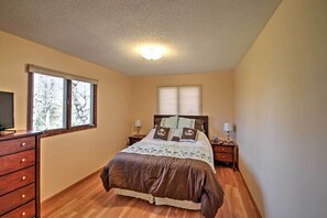 Une chambre à coucher comprenant un lit, deux tables de chevet, une commode, une fenêtre et un luminaire au plafond.