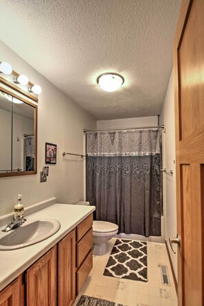 Une salle de bain équipée d’un lavabo, d’un miroir, de toilettes, d’un rideau de douche et d’un tapis à motifs.