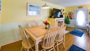 A dining area with a wooden table and chairs, a television, and a door with a curtain. - Condo w/ Deck: Walk to Beach & Convention Center! (Wildwood)