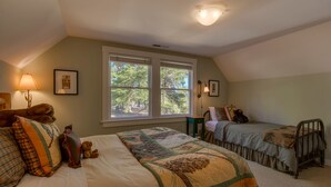 Une chambre avec deux lits, une fenêtre donnant sur des arbres, une lampe et un ours en peluche.