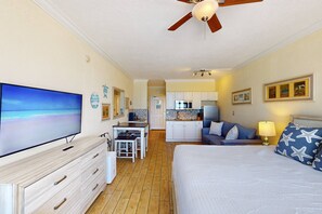 Une chambre dotée d’un lit, d’une télévision, d’un ventilateur de plafond, d’un coin cuisine et offrant une vue sur la plage.